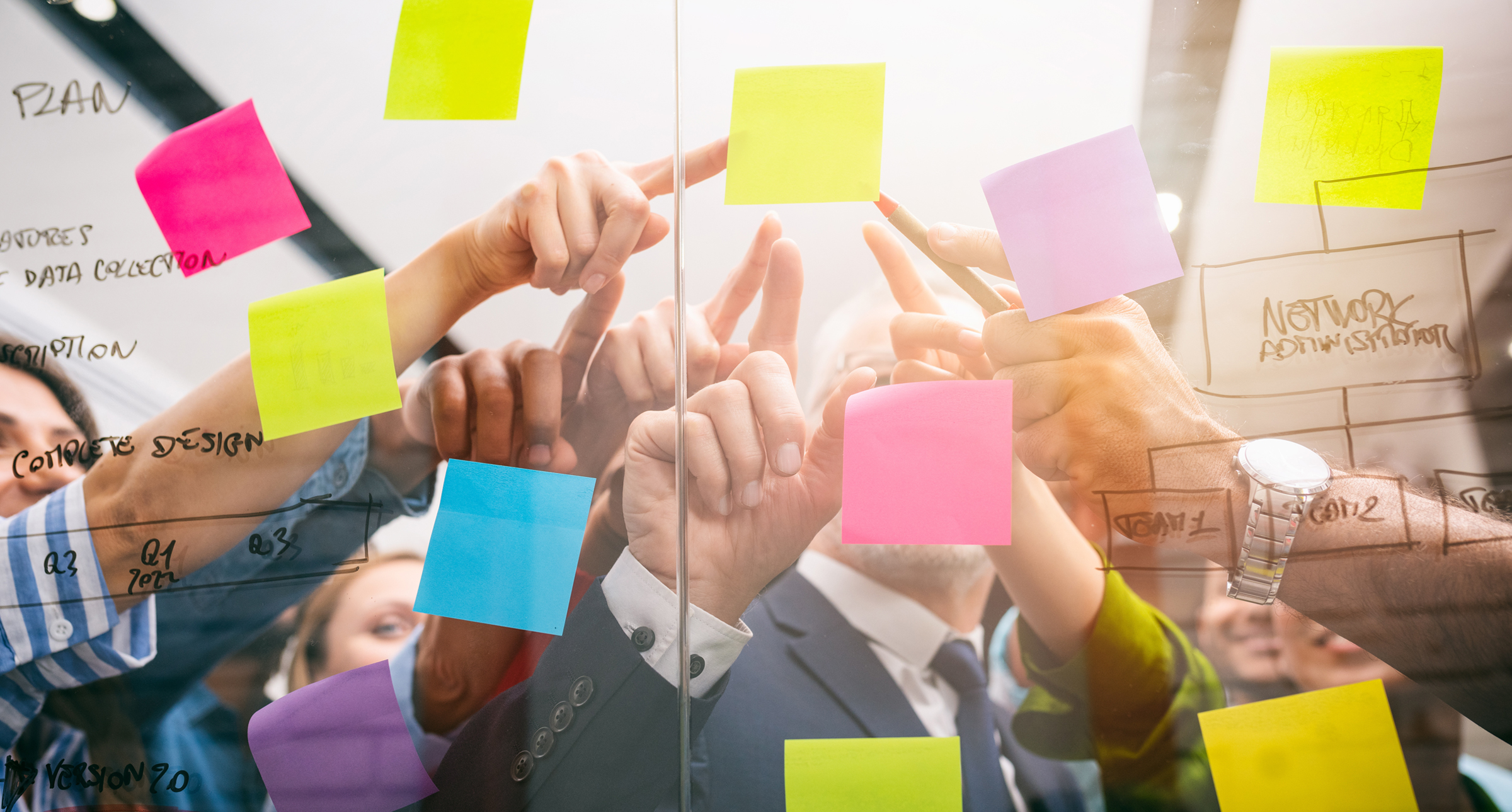 People pointing to a transparent whiteboard covered in post it notes.