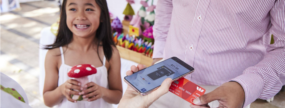 Little girl holding a mushroom toy while dad tapping to pay with EFTPOS Air