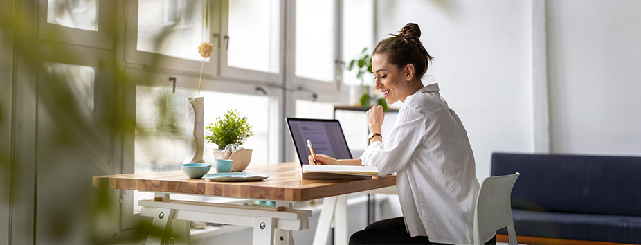 A young woman with light skin tone is sitting at a desk, working on a laptop in a studio. 