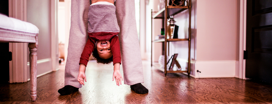 A child with light skin tone is being held upside down with their arms over their head. They have a big smile. 